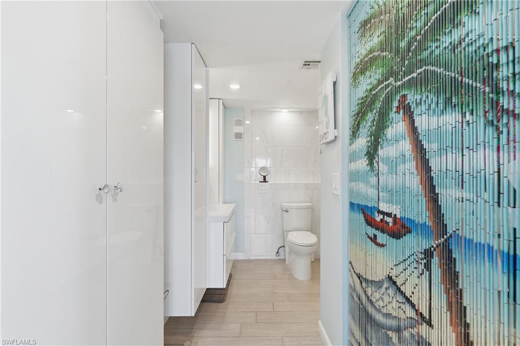 Modern bathroom featuring a spacious walk-in shower with glass enclosure, dual vanity sinks, toilet, and wood-finish flooring throughout - Virtually Edited Image