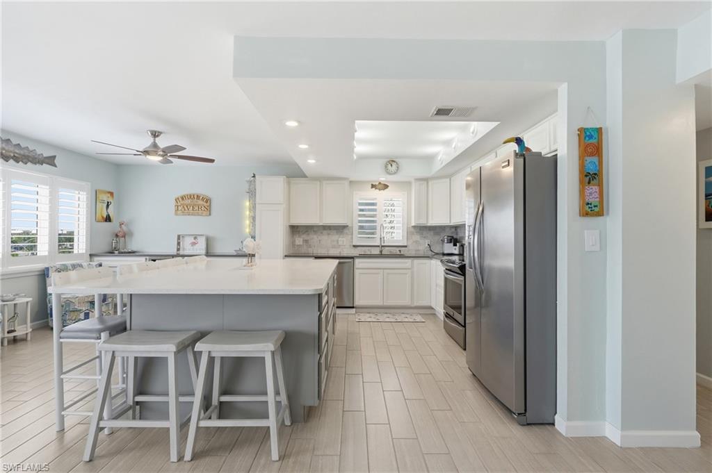 Kitchen featuring a large central island, white cabinetry, integrated stainless steel appliances, and wood-finish flooring - Virtually Edited Image