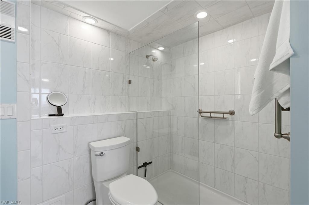 Modern bathroom featuring clean white subway tile walls, a frameless glass shower enclosure with brushed nickel hardware, a low-profile toilet, and recessed ceiling lighting - Virtually Edited Image