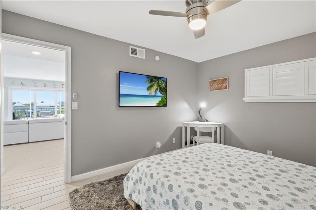 Serene secondary bedroom featuring soft gray walls, a ceiling fan with integrated lighting, white built-in cabinetry, and plush carpeting - Virtually Edited Image