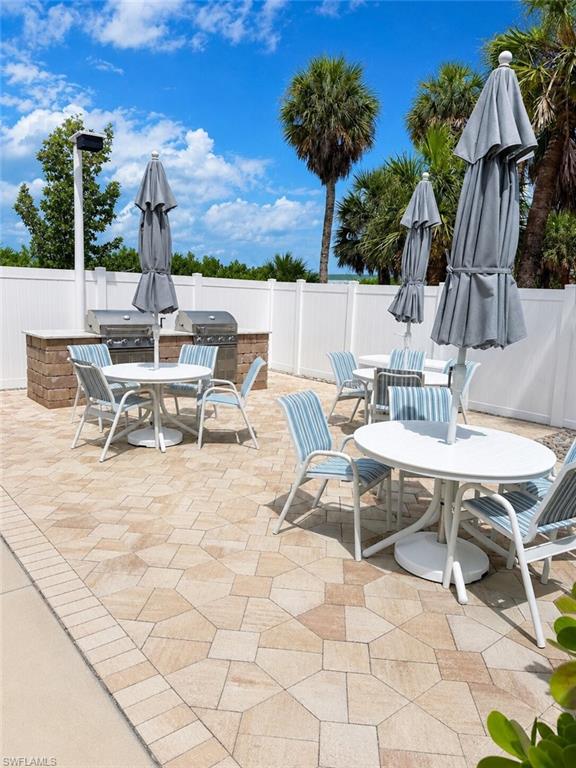 Expansive paver patio with a built-in outdoor kitchen, multiple grill stations, and a white privacy fence - Virtually Edited Image