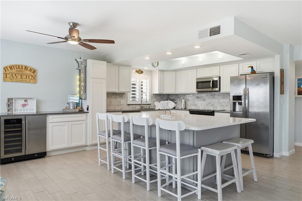 Chef's kitchen featuring custom white cabinetry, stainless steel appliances, quartz countertops, and a spacious island with seating for multiple guests - Virtually Edited Image