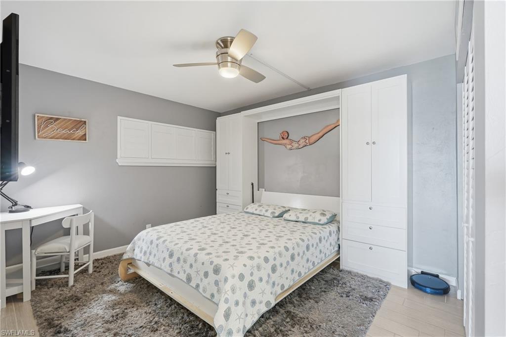 Spacious bedroom featuring a white canopy bed frame, soft-finish area rug, ceiling fan with brushed nickel fixture, gray accent walls, and ample natural light from windows - Virtually Edited Image