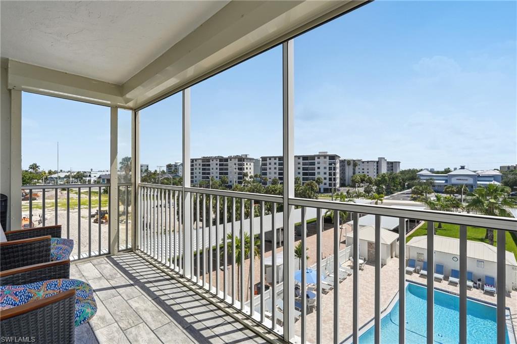 Expansive covered balcony with floor-to-ceiling glass panels and white metal railing, offering unobstructed sightlines to the resort-style pool, manicured grounds, and surrounding residential community - Virtually Edited Image