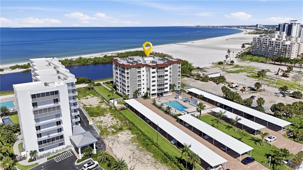Beachfront residential complex featuring multiple contemporary mid-rise buildings with direct oceanfront access, resort-style amenities including lagoon-style pools, manicured landscaping with mature palms, and expansive sandy beach frontage - Virtually Edited Image