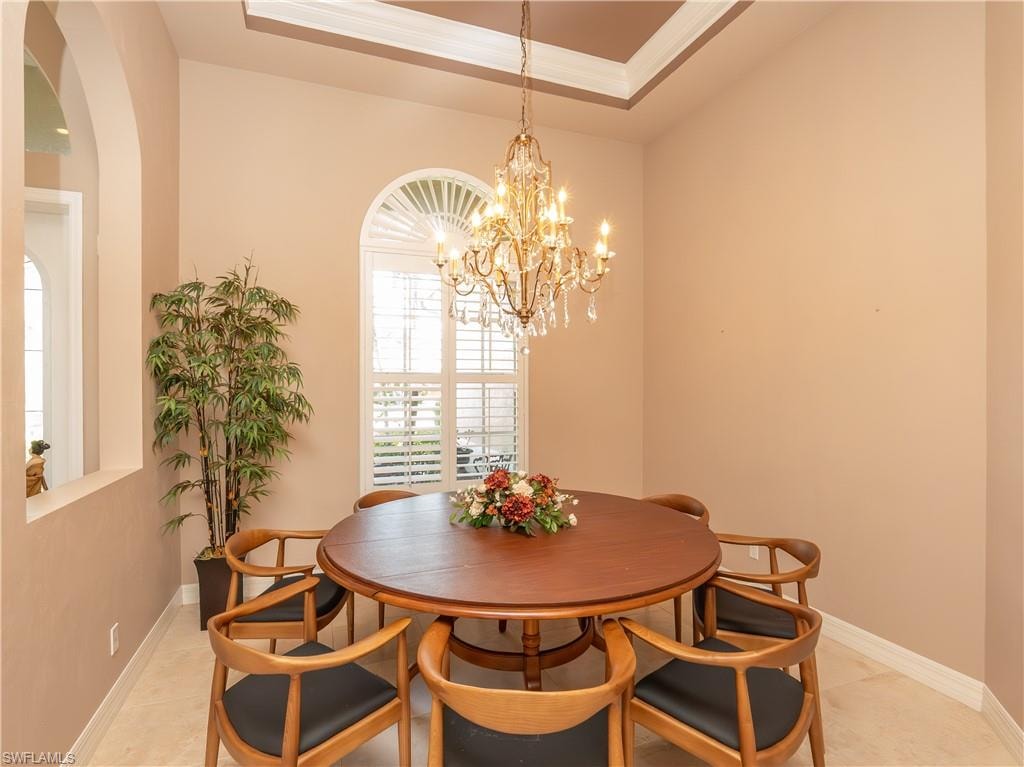 Tray ceiling with crown molding, crystal chandelier, arched window with plantation shutters, arched wall opening, and tile flooring