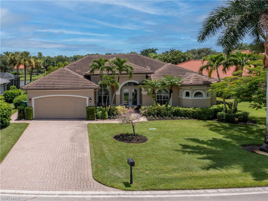 Stucco exterior with a tile roof, arched entryway, brick paver driveway, and mature landscaping