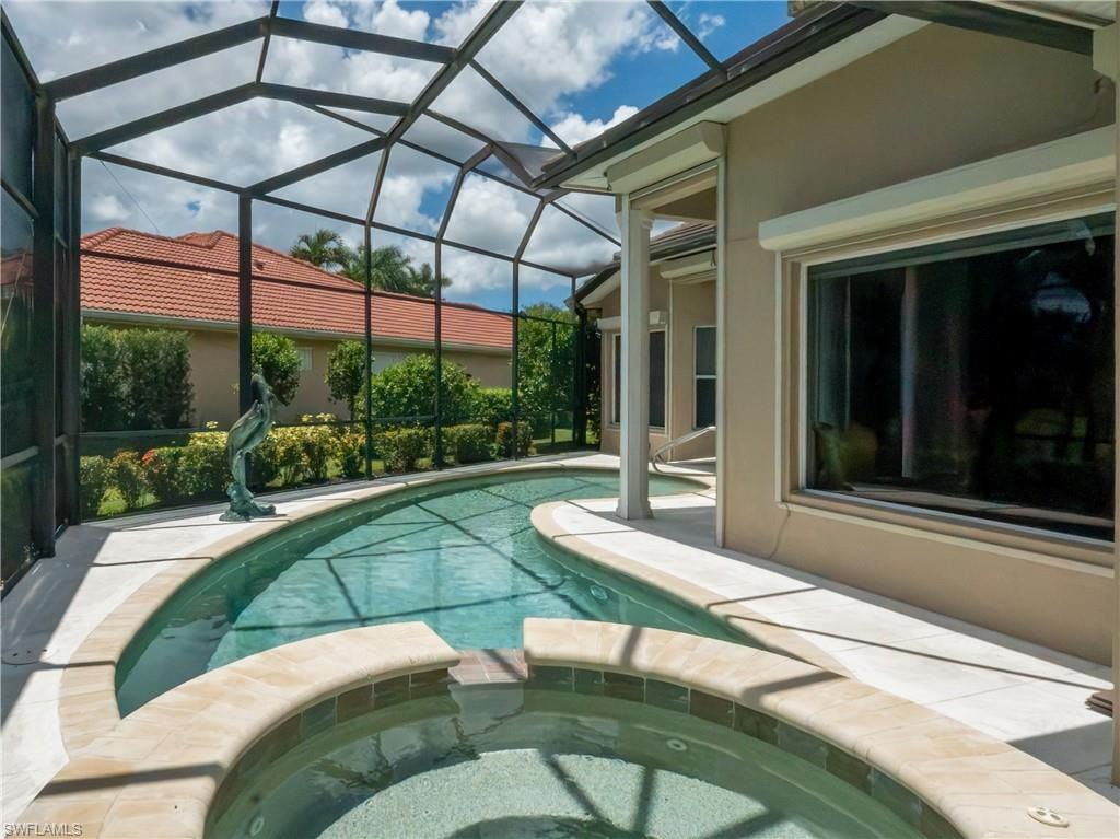 Screened lanai featuring a built-in spa, freeform pool, and a stucco exterior