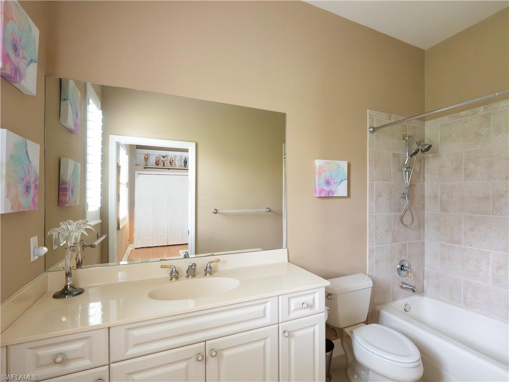 Bathroom featuring a built-in vanity with an integrated sink, a large wall-mounted mirror, a tiled shower-over-tub, and a toilet
