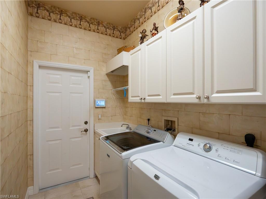 White cabinetry with brushed nickel hardware, utility sink, and tiled walls