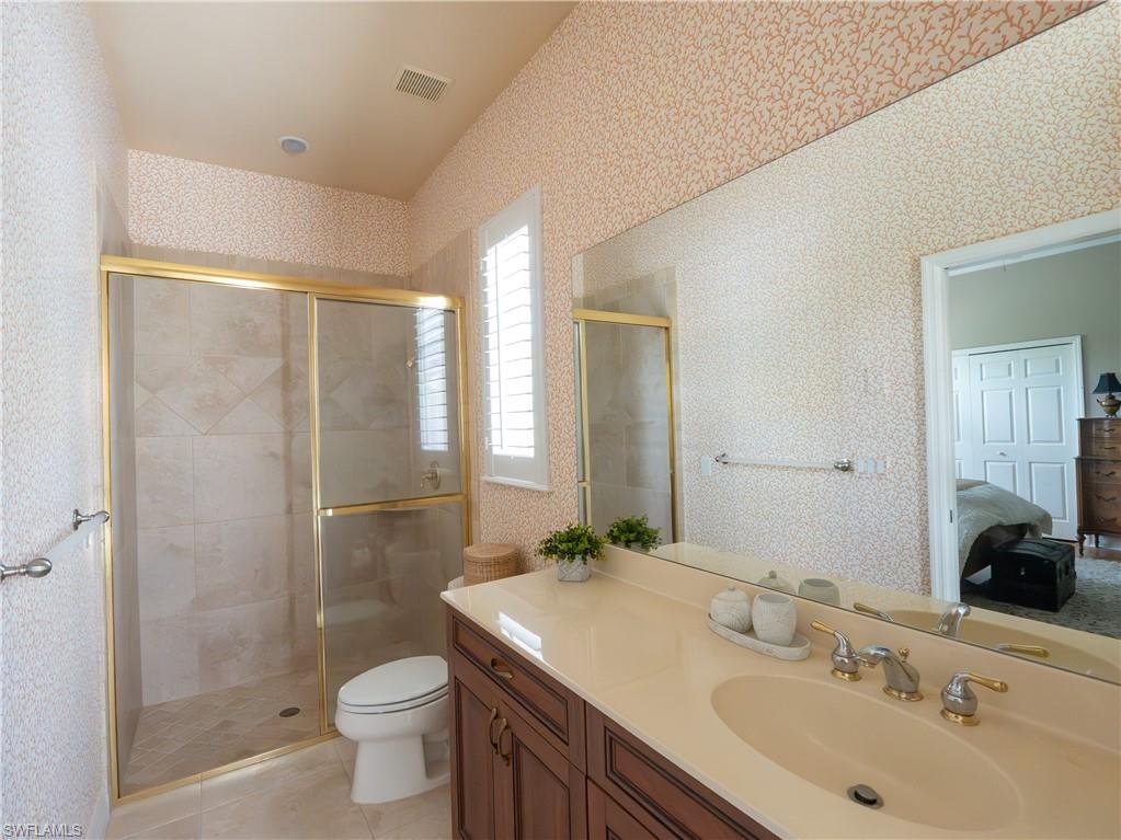 Tiled shower with a gold-finish glass enclosure, single vanity with an integrated sink, and white plantation shutters