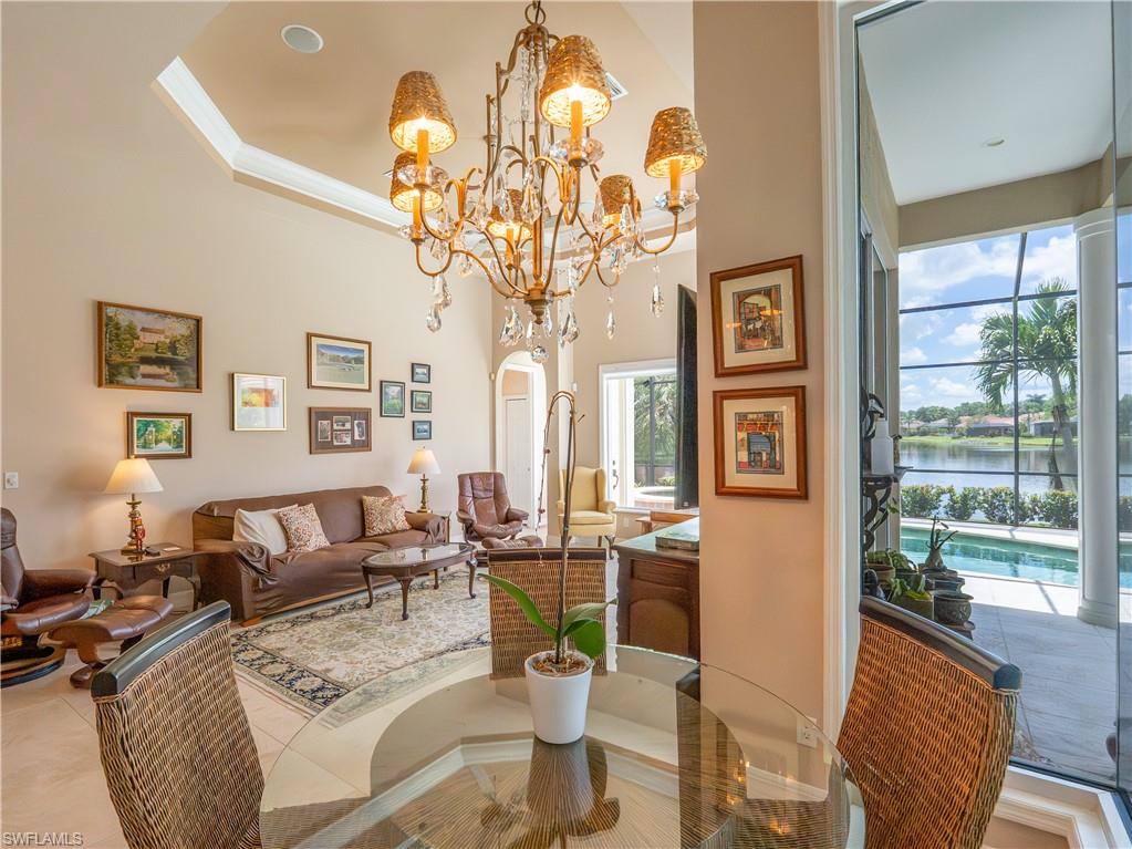 Tray ceiling detail with crown molding, chandelier with crystal accents, glass-top dining table, large sliding glass doors, and a screened lanai with a swimming pool