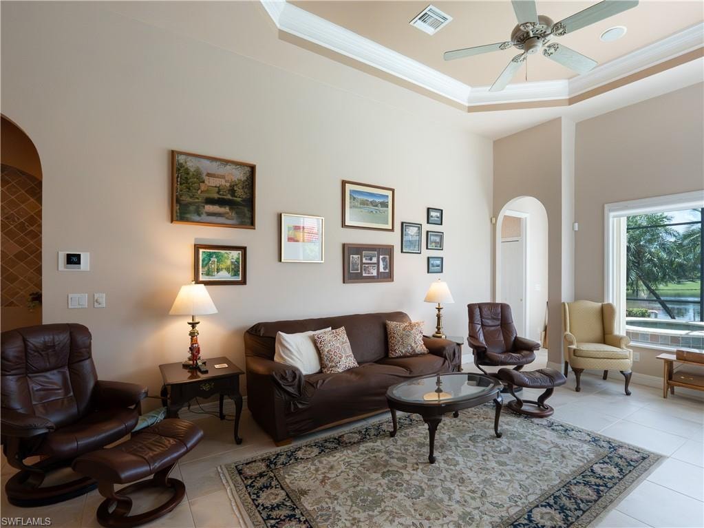 Tray ceiling with crown molding, ceiling fan, arched doorways, tiled flooring, and expansive windows