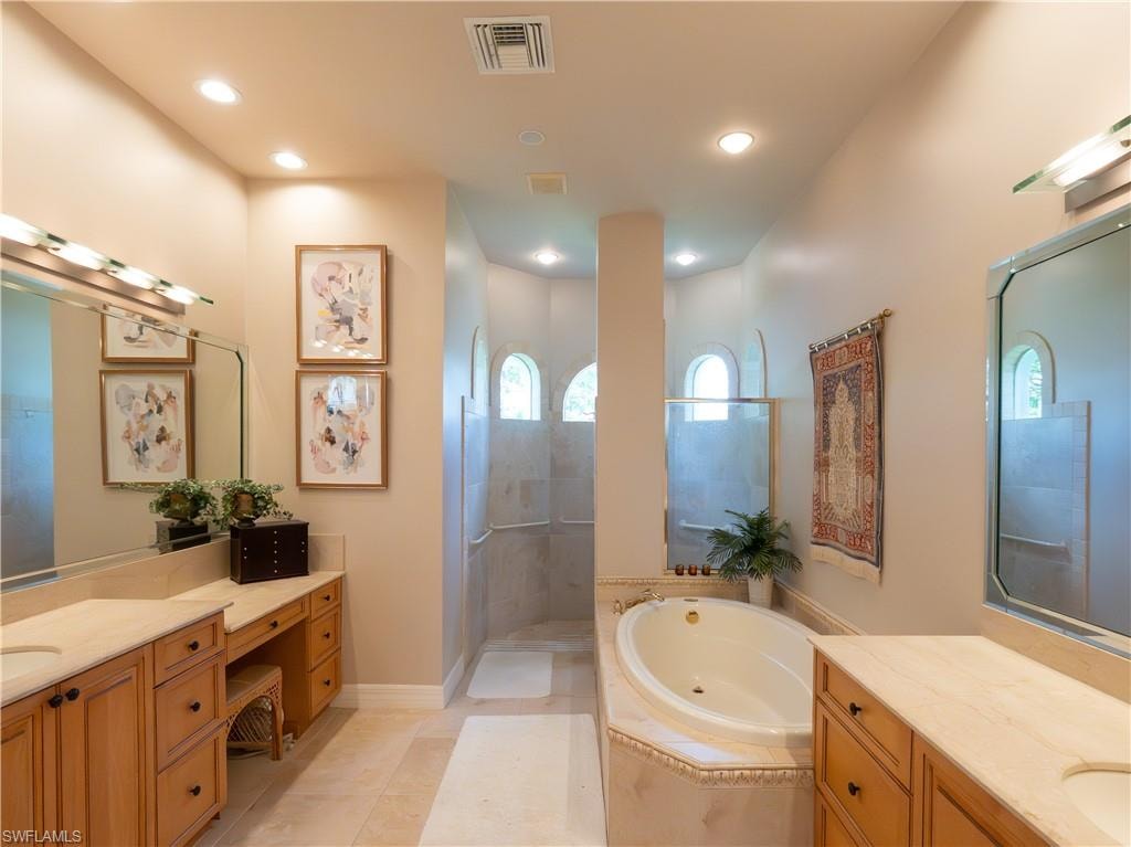 Dual vanity with wood-finish cabinetry and integrated sinks, a built-in makeup counter, a corner soaking tub, and a separate walk-in shower with arched window accents