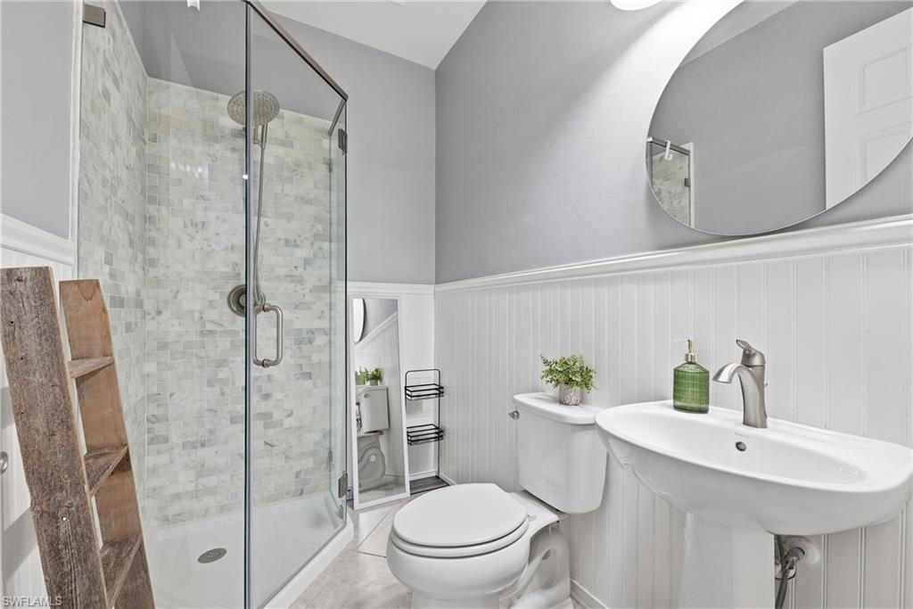 Glass-enclosed shower with subway tile surround, pedestal sink with brushed nickel faucet, and a wall-mounted oval mirror