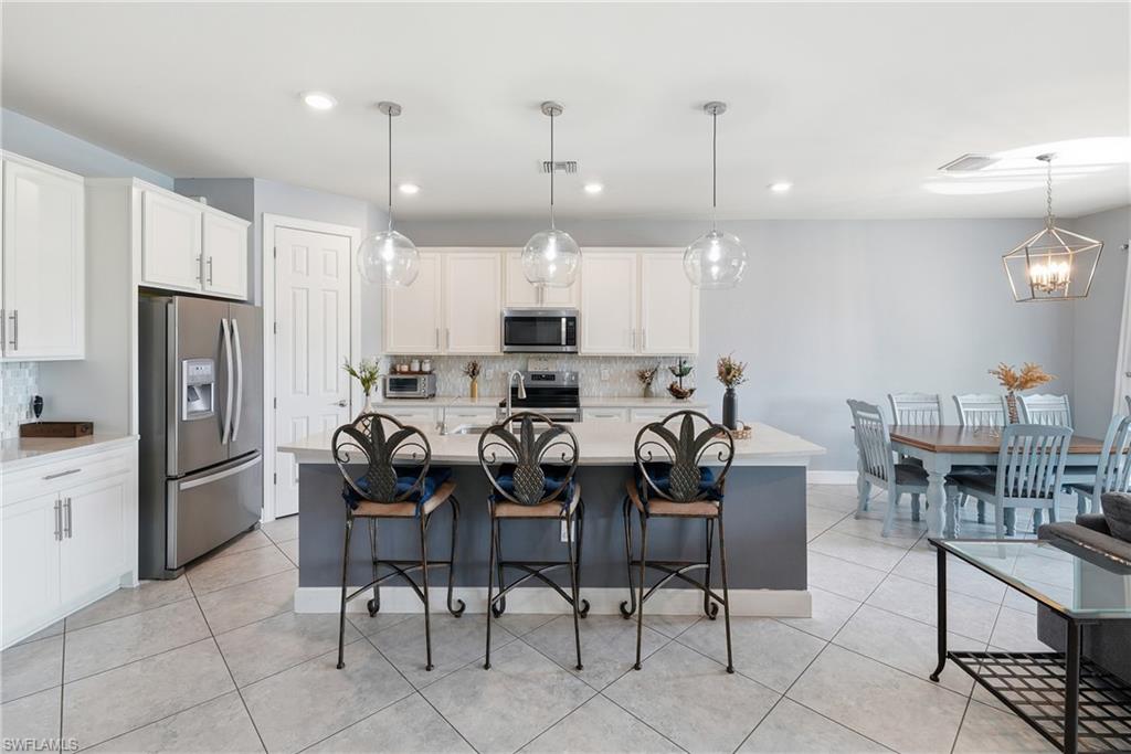 Open-concept kitchen and dining area featuring a central island, white cabinetry, stainless steel appliances, and tile flooring