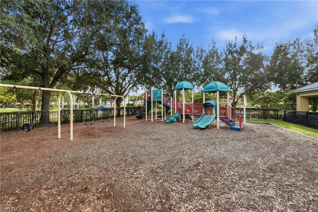 Community playground featuring a multi-level play structure with slides and stairs, a swing set, and a wood chip surface