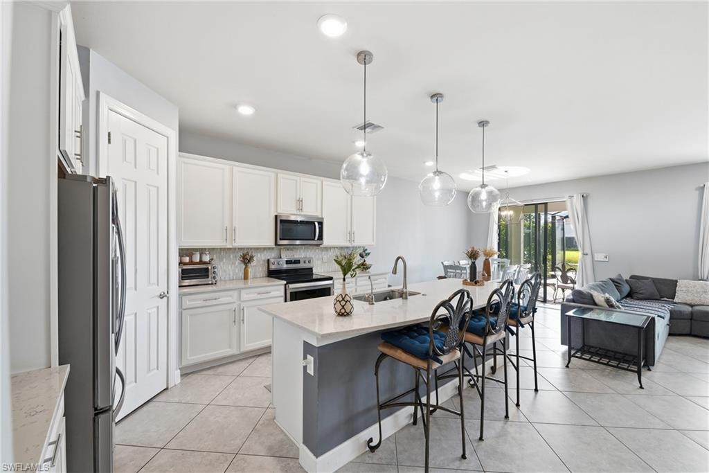 Open-concept kitchen featuring white cabinetry, stainless steel appliances, and a central island with a sink