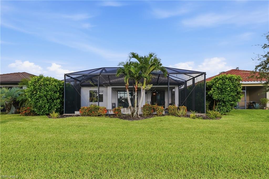 Expansive rear lawn featuring a screened lanai, mature landscaping, and an exterior of light-colored stucco