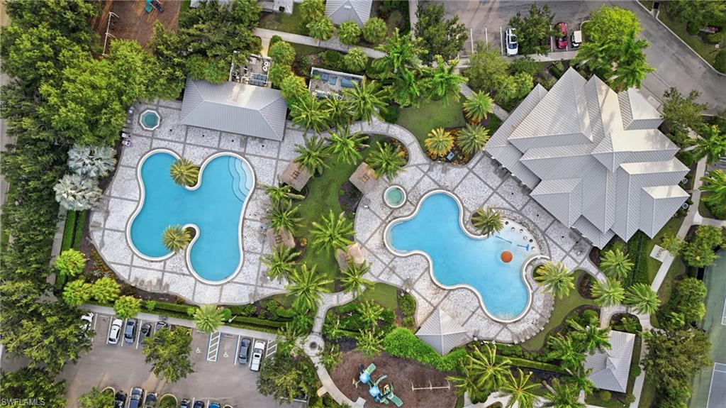 Aerial view showcasing two resort-style swimming pools with curved, organic shapes and sun shelves, surrounded by lush tropical landscaping, mature palms, and expansive hardscaped entertaining areas