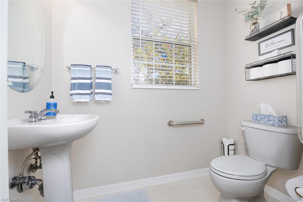 Pedestal sink with chrome faucet, oval wall-mounted mirror, and ceramic toilet