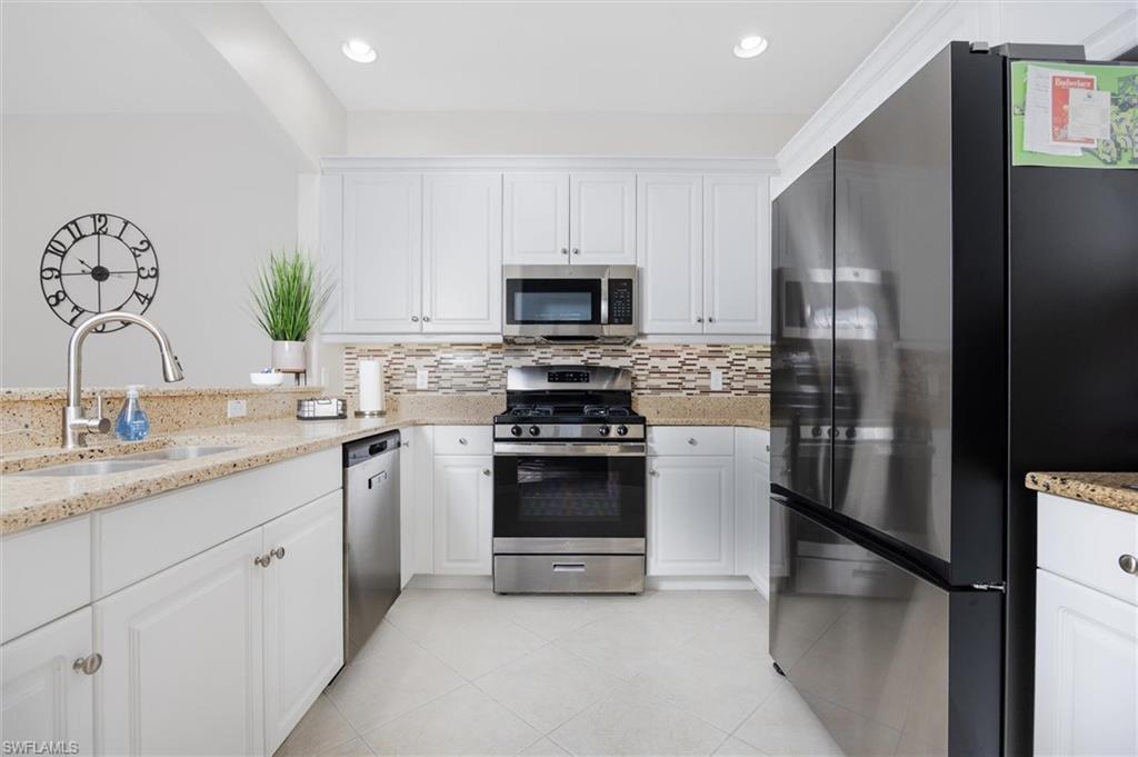 Kitchen featuring white cabinetry, light-toned countertops, a mosaic tile backsplash, stainless steel appliances, and tile flooring