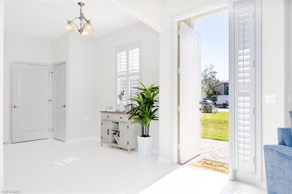 Bright entry foyer featuring a chandelier, white paneled doors, and plantation shutters