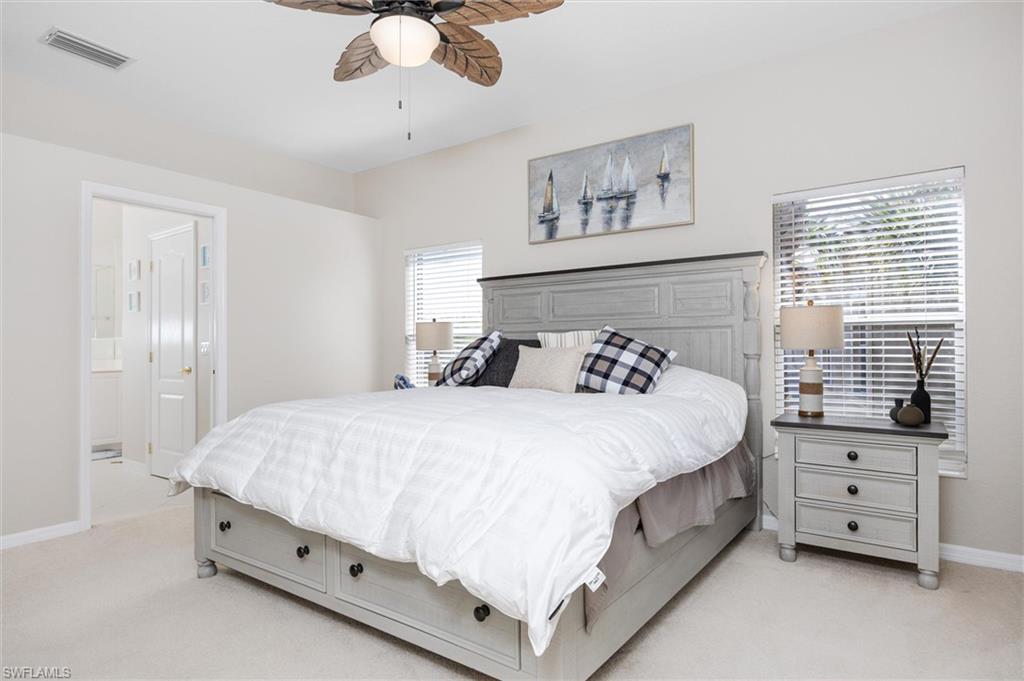 Carpeted bedroom featuring a ceiling fan with light fixture, a window with blinds, and an open doorway revealing a bathroom with a white vanity
