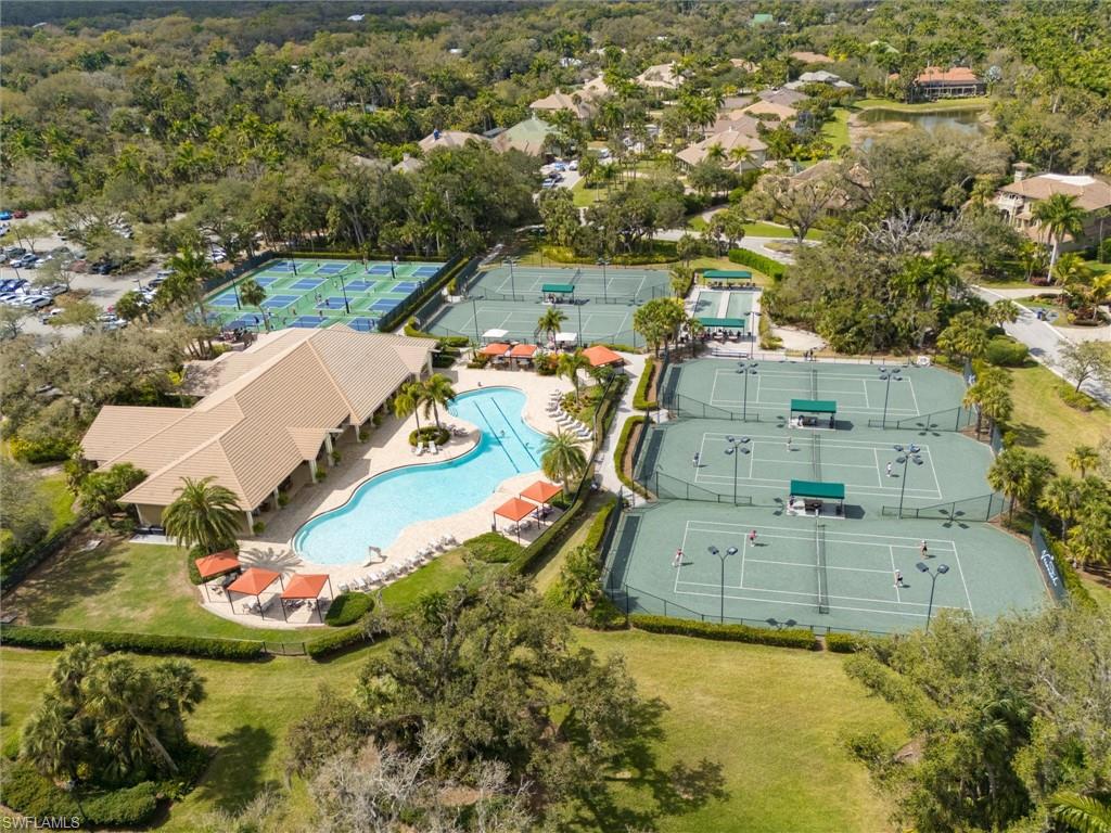 Community amenities featuring a clubhouse with a barrel tile roof, a lagoon-style swimming pool, surrounding lounge areas with orange umbrellas, multiple tennis courts, and numerous pickleball courts