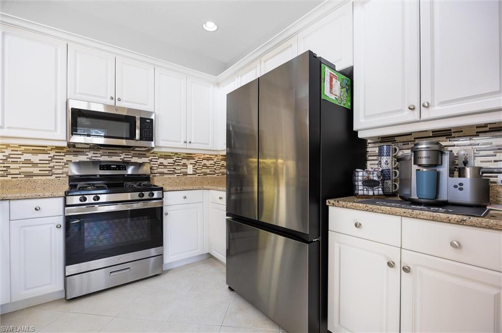 Kitchen featuring white cabinetry, stainless steel appliances, speckled stone countertops, and a mosaic tile backsplash