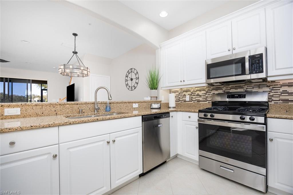 Kitchen featuring white cabinetry, speckled countertops, stainless steel appliances, and a mosaic tile backsplash