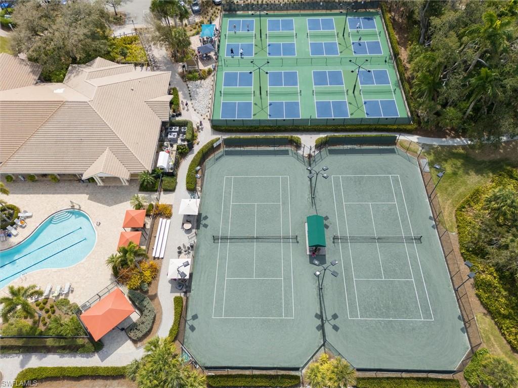 Expansive recreational area featuring a large swimming pool, two tennis courts with fencing and lighting, and multiple pickleball courts with fencing