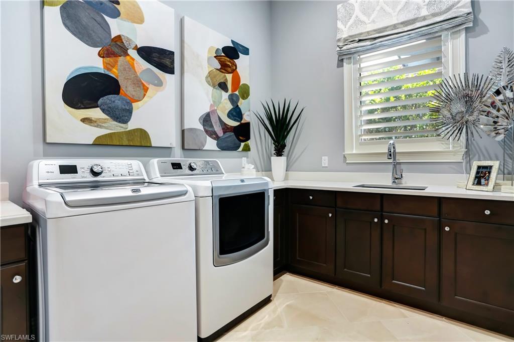 Laundry room featuring dark wood-finish cabinetry with white hardware, light-toned countertop, and an integrated sink with a gooseneck faucet
