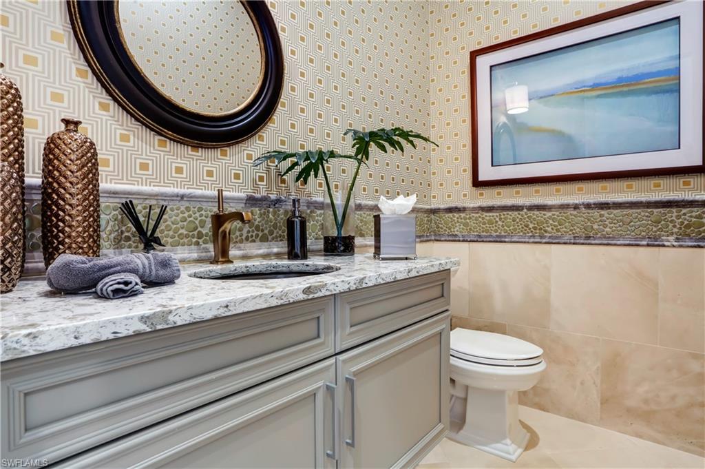 Powder room featuring a gray vanity with a stone countertop and an oval black-framed mirror