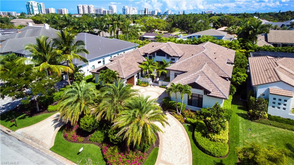 Spacious property featuring a tiled roof, paver driveway, mature palm trees, manicured lawns, and lush landscaping