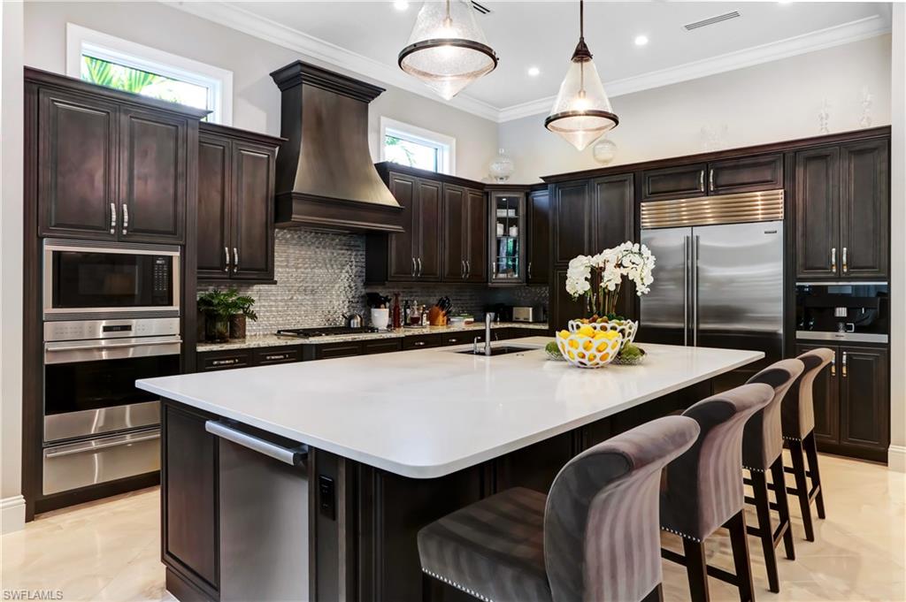 Spacious kitchen featuring dark wood cabinetry, a large center island with a light-toned countertop, and integrated stainless steel appliances including a double oven and refrigerator