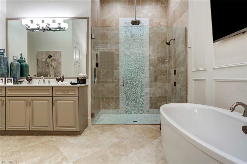 Spacious bathroom featuring a freestanding soaking tub, a walk-in shower with dual shower heads and mosaic tile detailing, a double vanity with a large mirror, and paneled wall trim