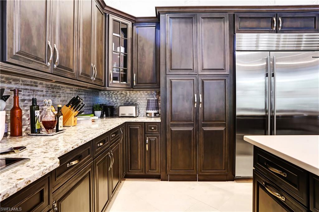 Kitchen featuring dark wood-finish cabinetry, light-colored stone countertops, a mosaic tile backsplash, and stainless steel appliances