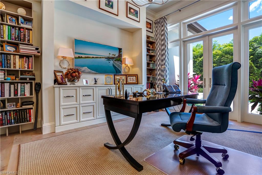 Dedicated office space featuring built-in shelving, custom cabinetry, wood-finish flooring, and expansive French doors opening to lush exterior landscaping