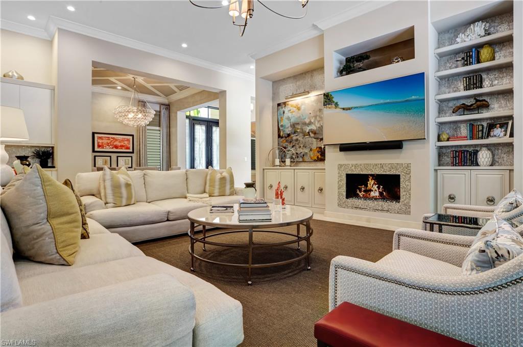 Living area featuring a gas fireplace with a stone surround, built-in shelving, recessed lighting, and crown molding