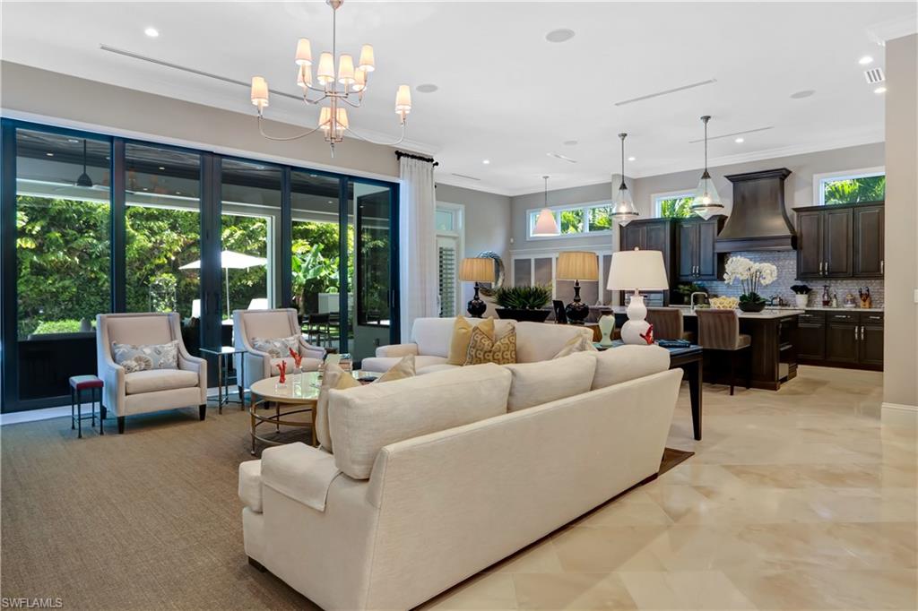 Expansive open-concept living area featuring large format tile flooring, a statement chandelier, and a kitchen with dark cabinetry, a range hood, and a tile backsplash