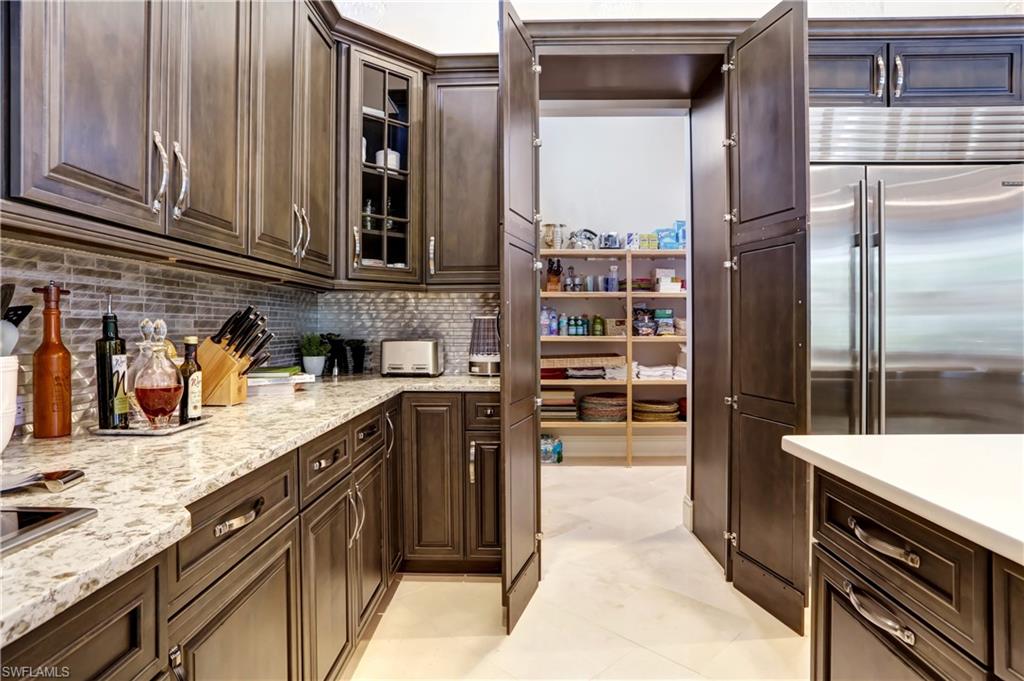 Kitchen featuring dark wood cabinetry, light speckled countertops, a tile backsplash, and a stainless steel refrigerator