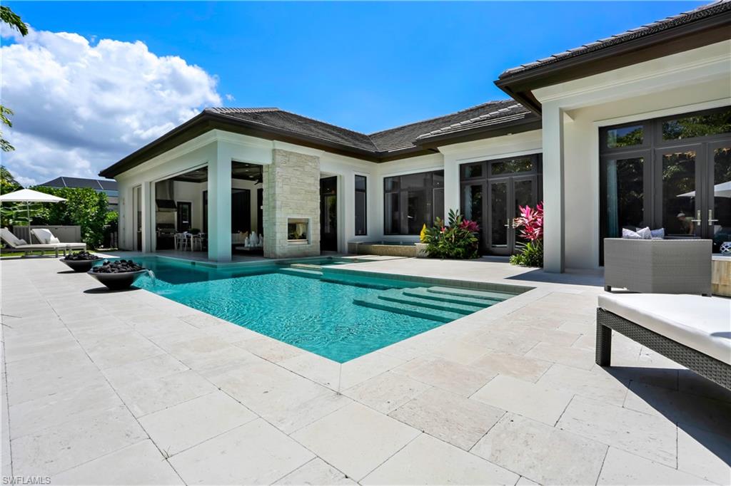 Expansive outdoor living area featuring a rectangular pool with integrated steps, a stone-clad exterior fireplace, and a spacious patio with large format pavers