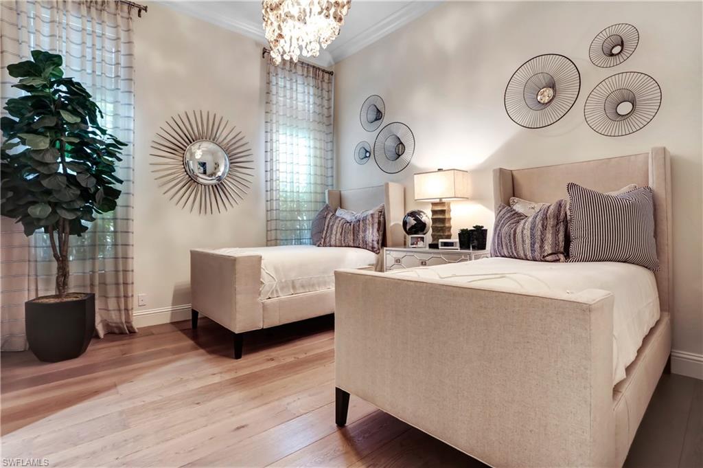 Room featuring wood-finish flooring, two upholstered beds with tall headboards, an overhead chandelier, and a built-in window with sheer curtains