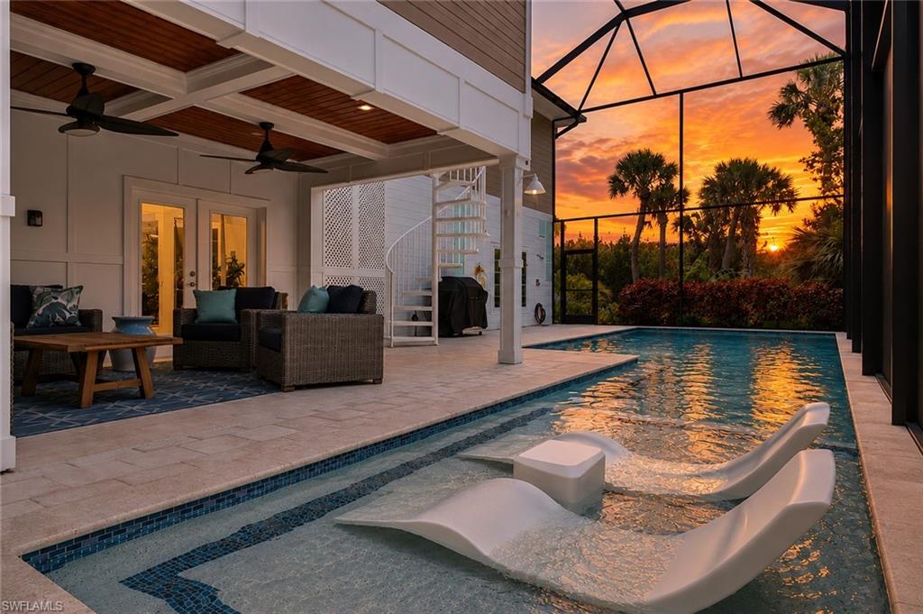 Screened swimming pool with integrated sun shelf and chaise lounges, featuring a spiral staircase, an overhead wood-paneled ceiling, and a covered patio area with dual ceiling fans