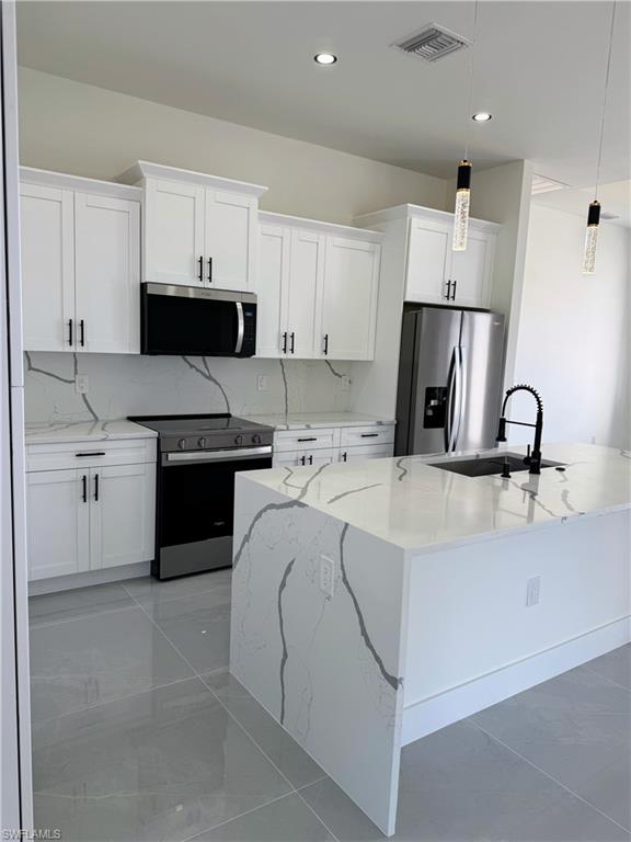 Modern kitchen featuring white shaker cabinetry with black hardware, stainless steel appliances, and sleek gray flooring
