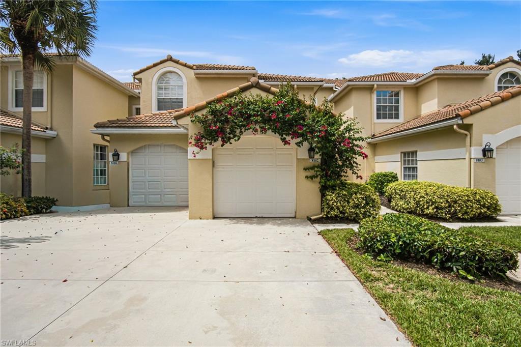 Elegant Mediterranean-inspired residence featuring a pristine concrete driveway, two-car garage with panel doors, and cream stucco exterior with clay tile roofing
