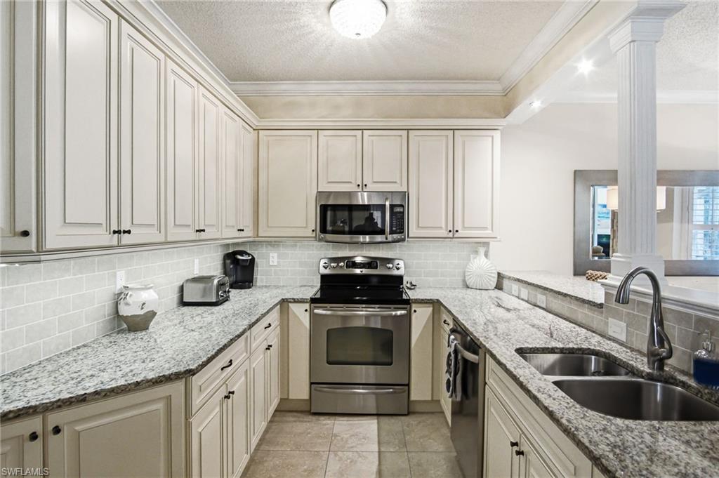 U-shaped kitchen featuring white cabinetry, light-colored countertops, a subway tile backsplash, stainless steel appliances, and tile flooring