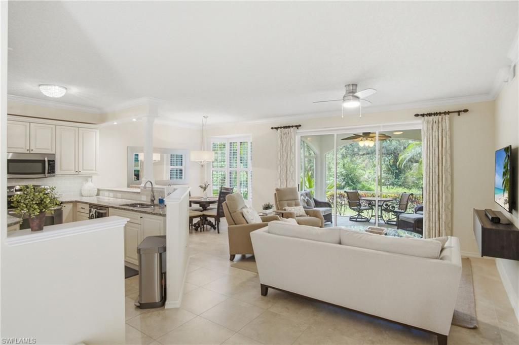Open-concept living and dining area featuring a white kitchen with stainless steel appliances, tile flooring, and abundant natural light from expansive sliding glass doors and windows