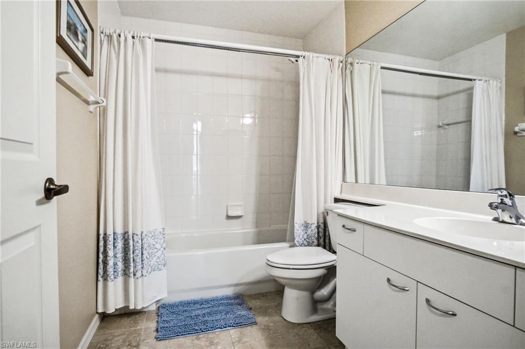 Bright and functional bathroom featuring a ceramic toilet, white vanity with dual sinks and chrome hardware, and a bathtub/shower combination with white subway tile surround and coordinating shower curtain